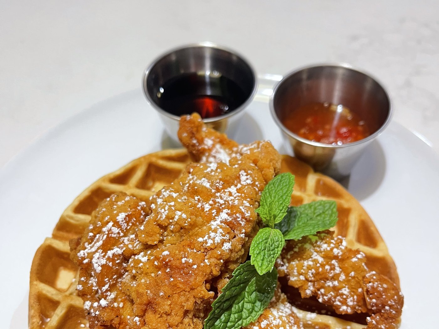 Fried chicken on a waffle with syrup and chili sauce