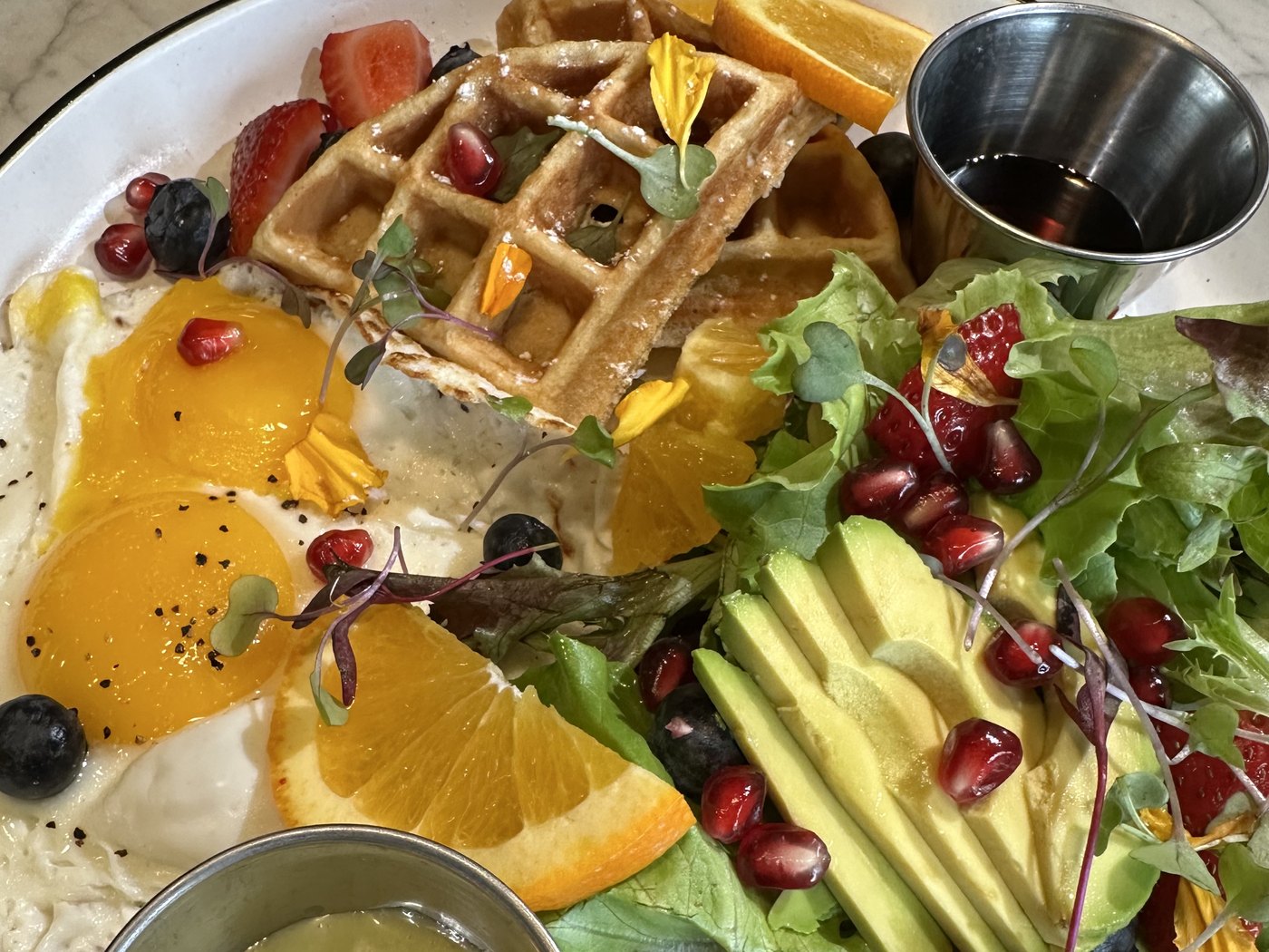 Breakfast plate with waffle, fried eggs, avocado salad, and fruit